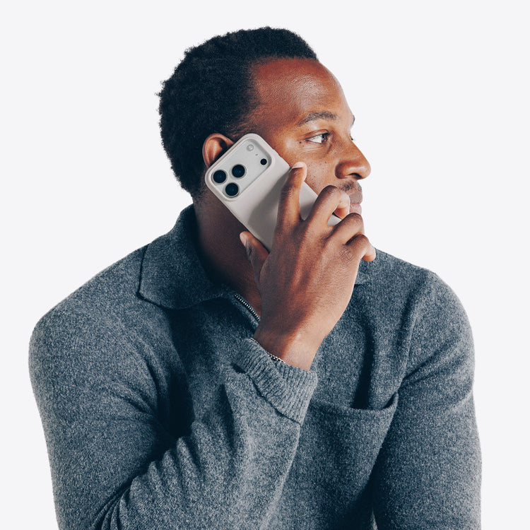 Man in gray sweater talking on a dune smartphone against a white background