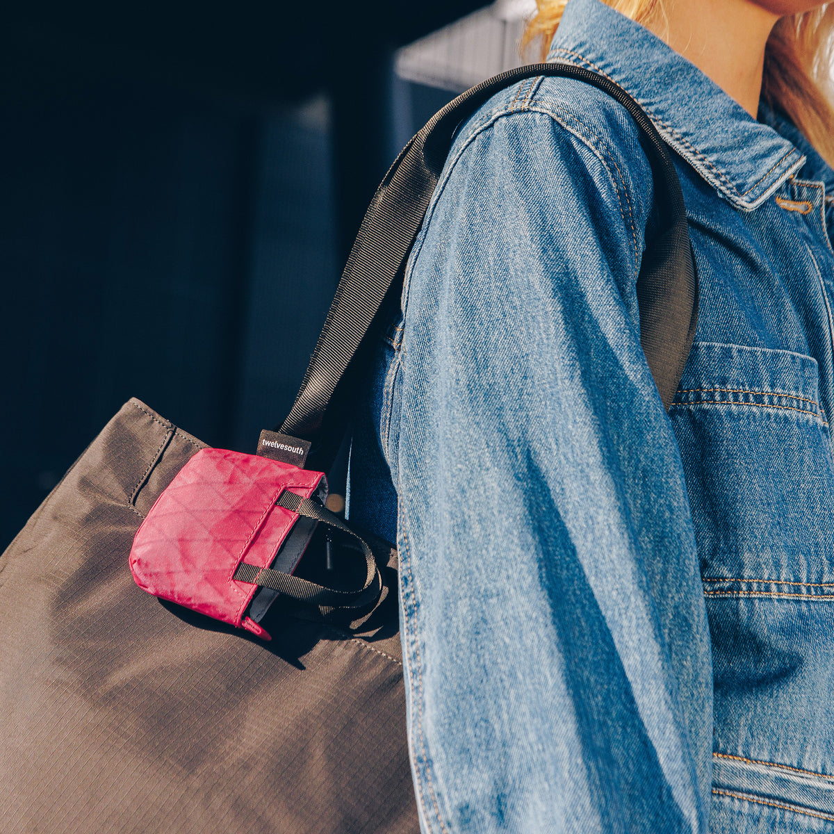 Person wearing a denim jacket with a brown bag and pink pouch over their shoulder.