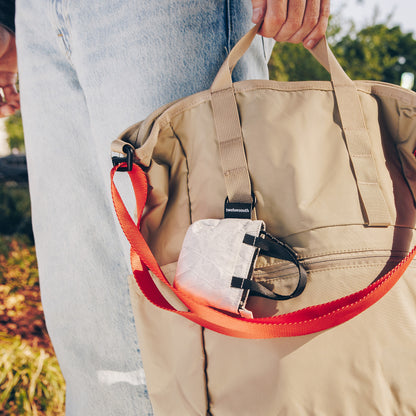 Person holding a beige bag with an orange strap, outdoors.