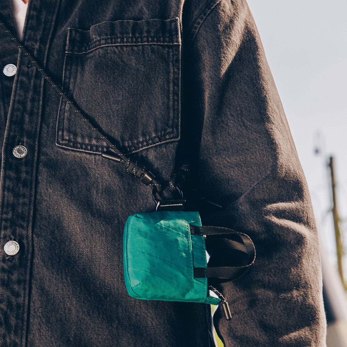 Person wearing a dark denim jacket with a green pouch attached to it.