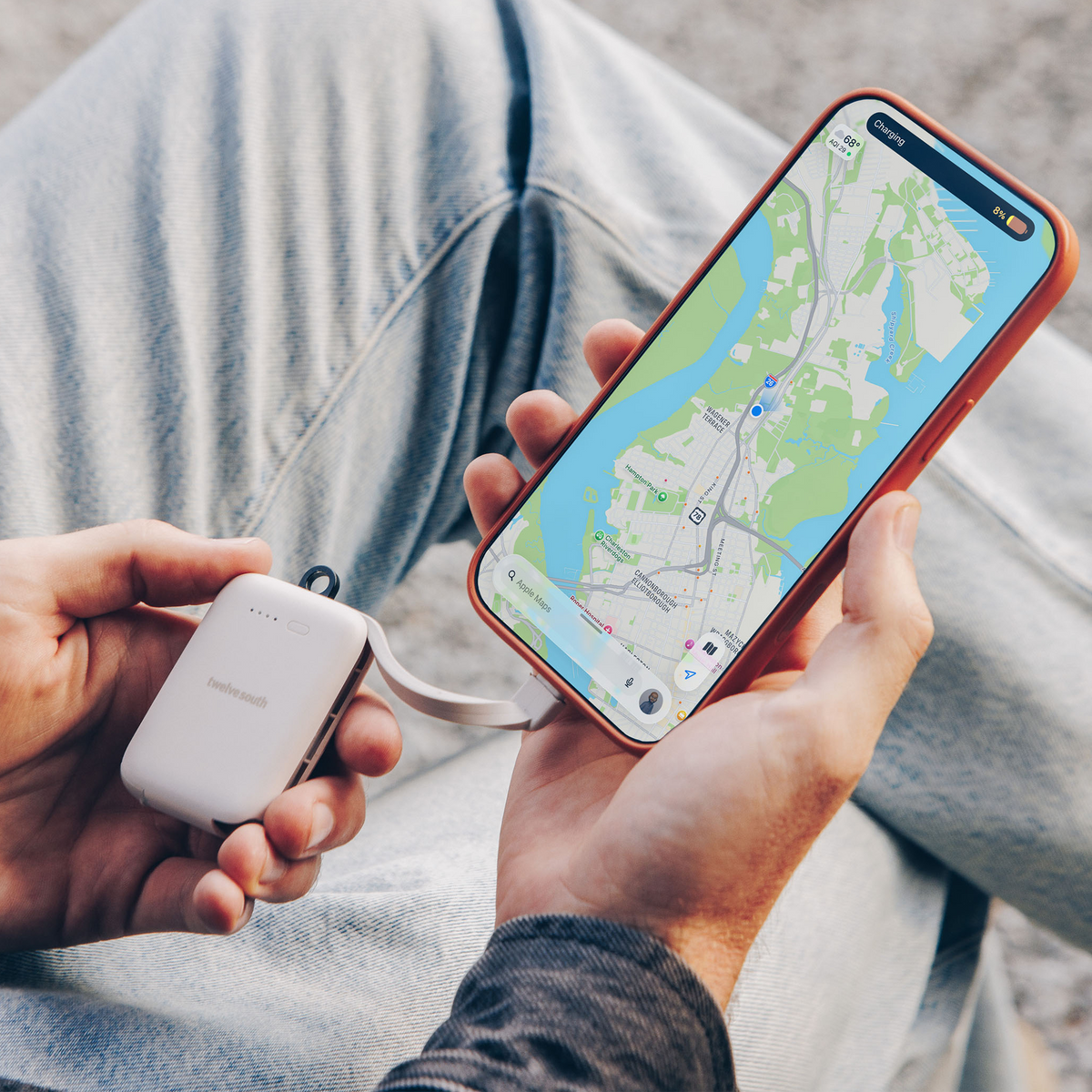 Person holding a phone with a map app and a white device, possibly a power bank, in their other hand.