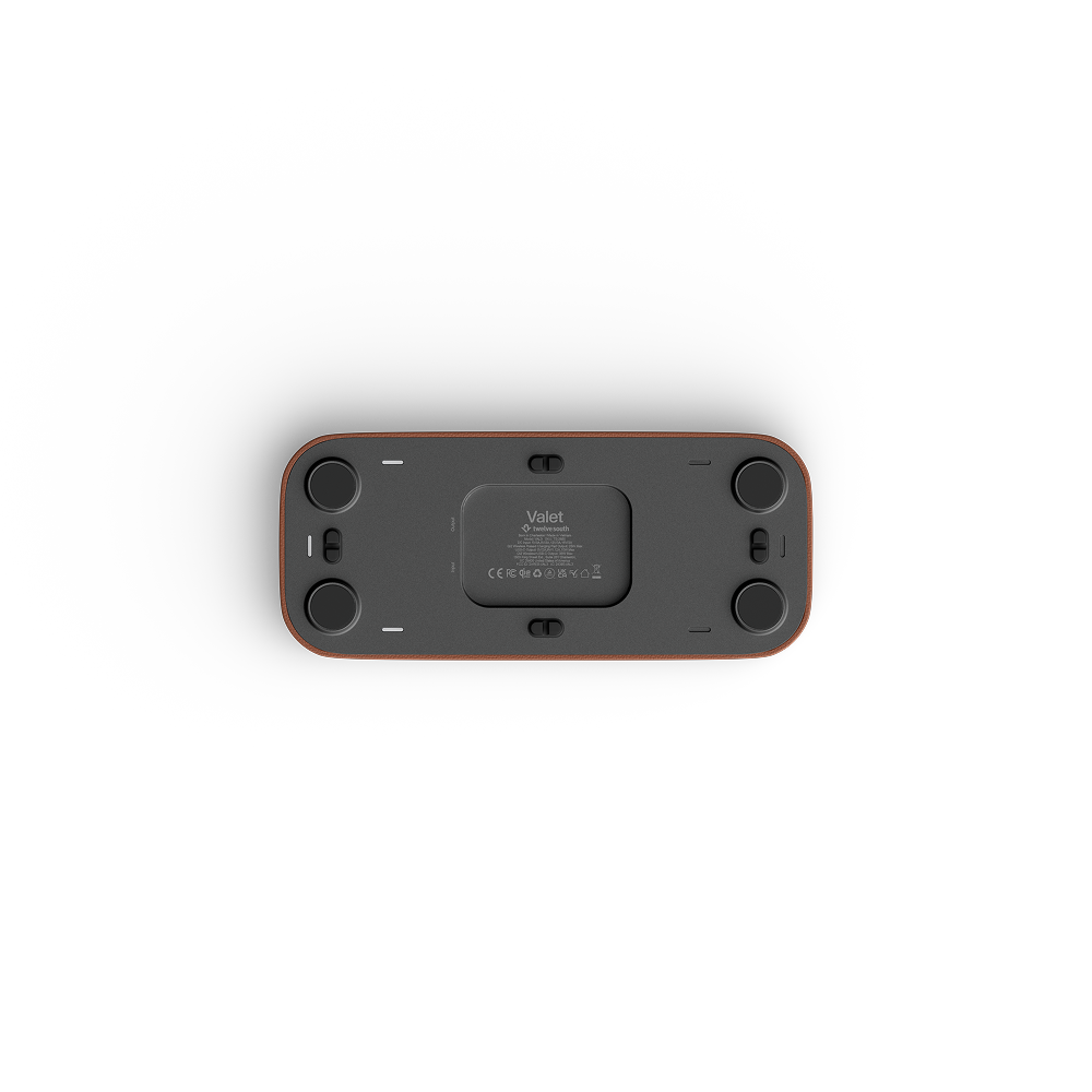 The bottom view of a valet device, showing a dark gray face with four black circular feet and a thin reddish-brown outer frame, on a solid white background.