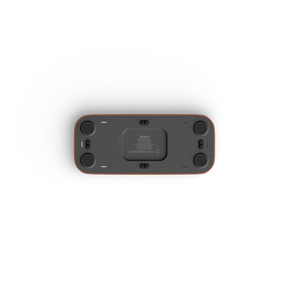 The bottom view of a valet device, showing a dark gray face with four black circular feet and a thin reddish-brown outer frame, on a solid white background.
